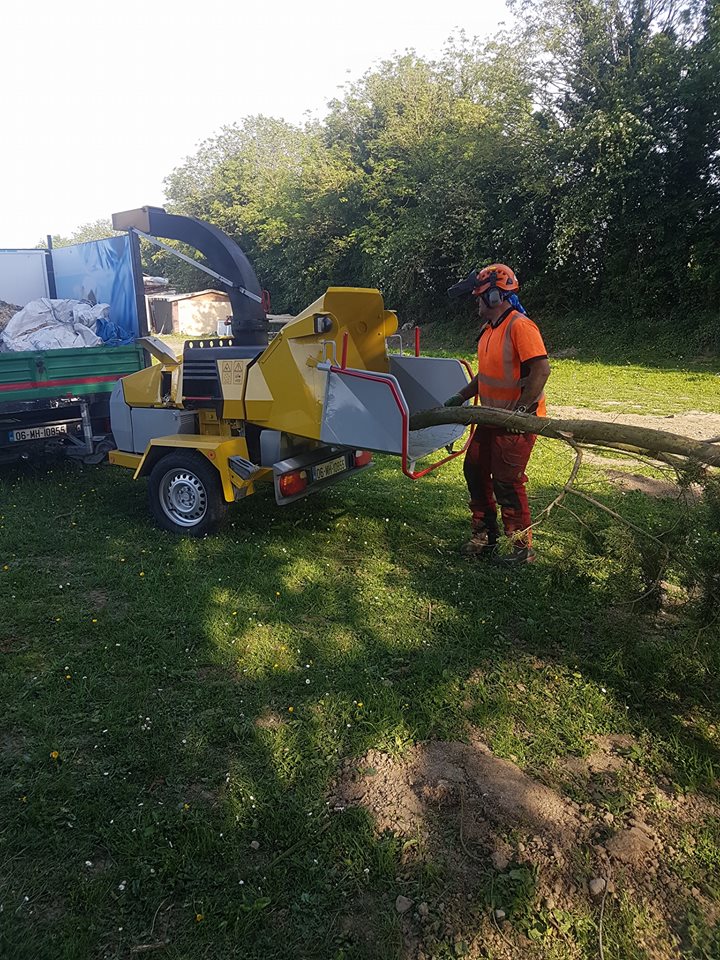 A tree surgeon in safety gear feeding branches into a wood chipper